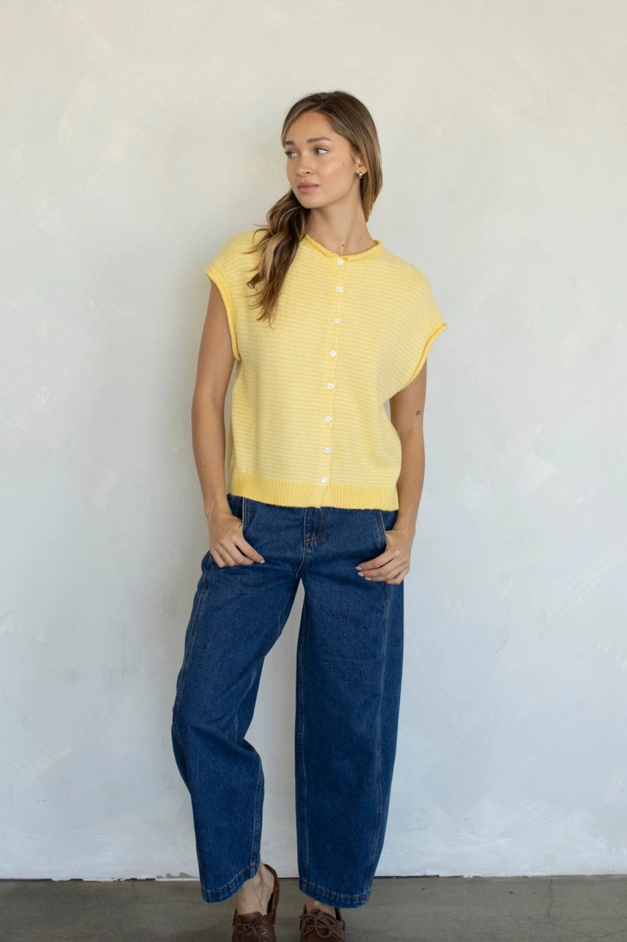 Woman wearing a yellow sleeveless top and blue jeans against a white wall