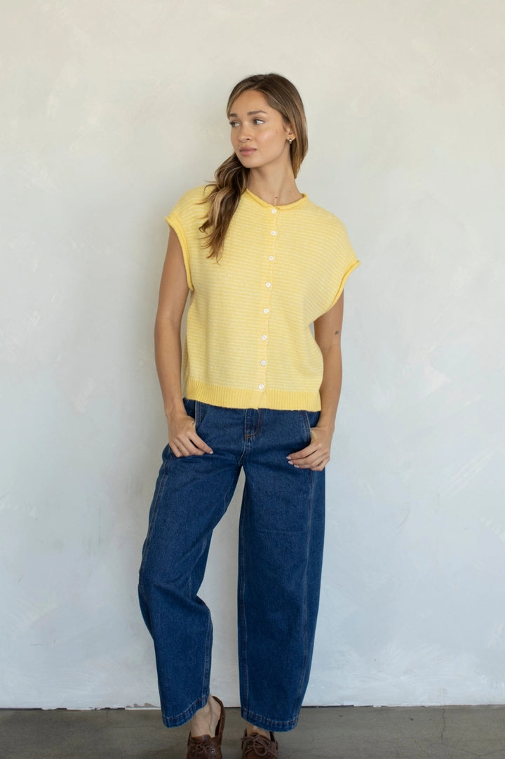 Woman wearing a yellow sleeveless top and blue jeans against a white wall