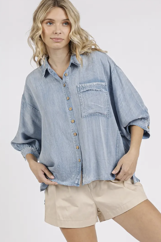 Woman wearing a light blue denim shirt and beige shorts on a white background