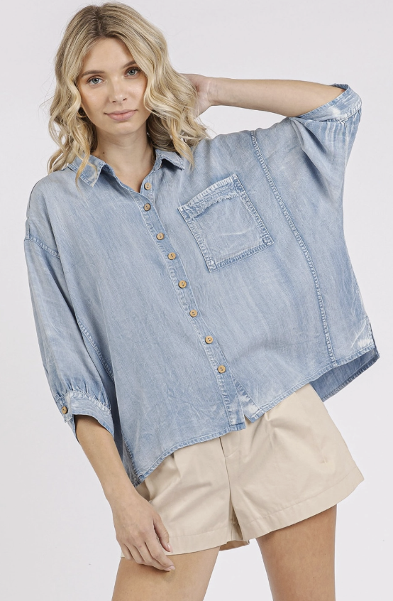 Woman wearing a light blue denim shirt with rolled-up sleeves on a white background
