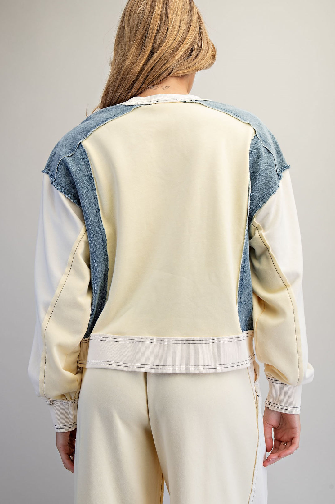 Person wearing a cream-colored sweatshirt with denim sleeves on a plain background
