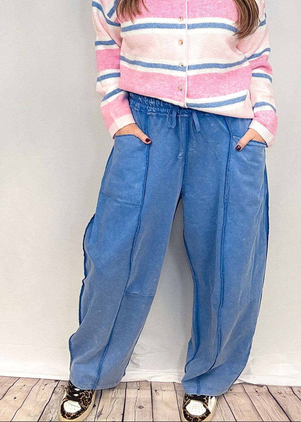 Woman wearing blue barrel sweatpants with pink and blue stripe cardigan on white background