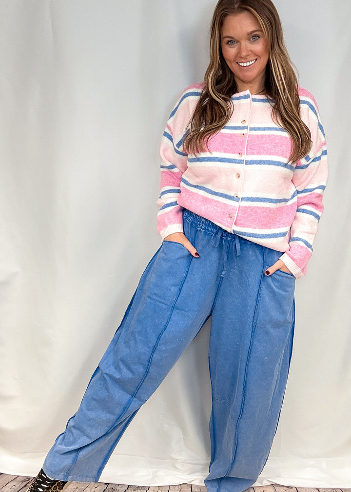 Woman wearing blue barrel sweatpants with pink and blue stripe cardigan on white background