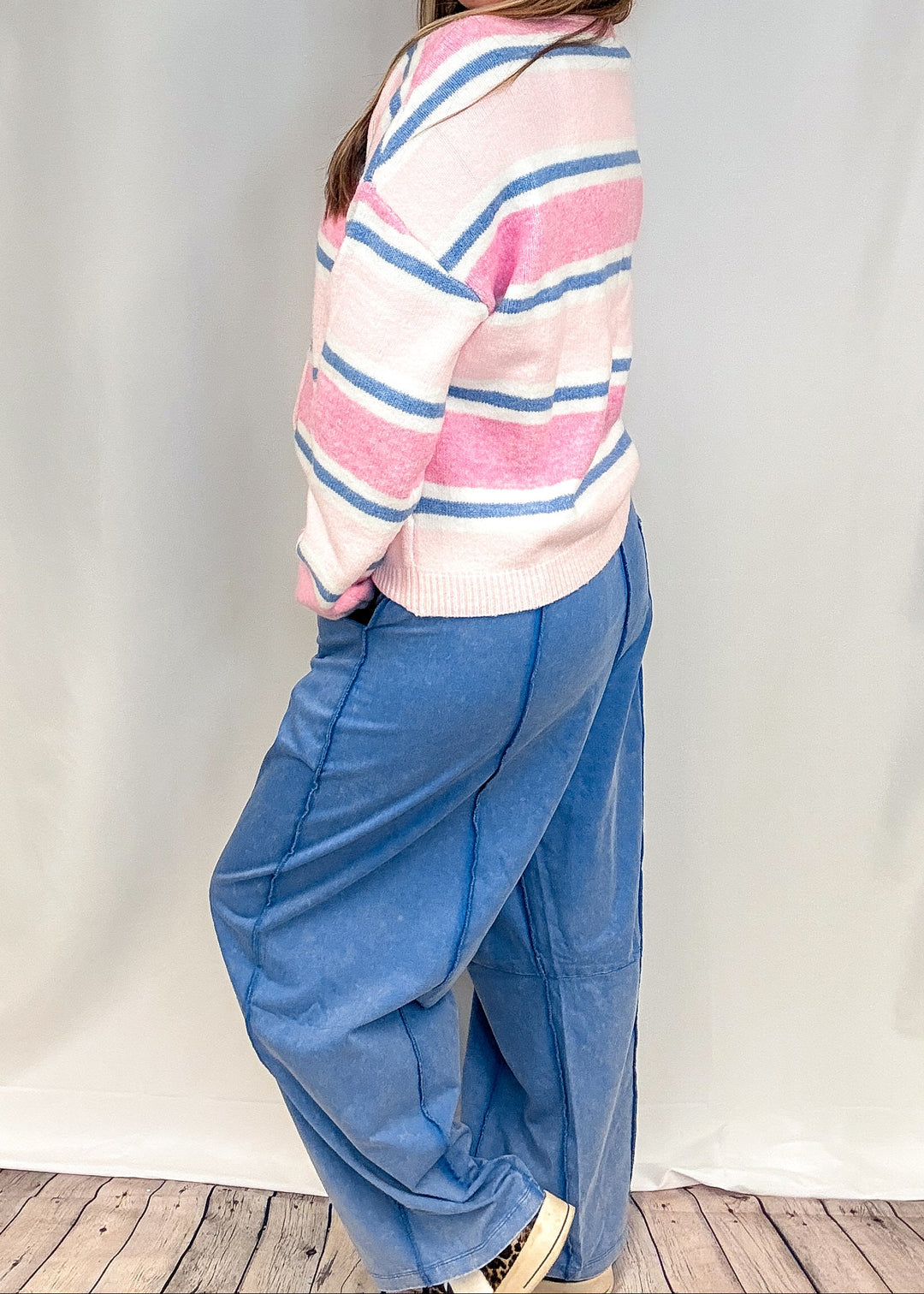 Woman wearing blue barrel sweatpants and pink and blue stripe cardigan on white background
