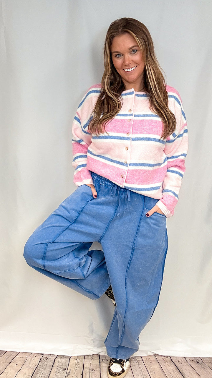 Woman wearing blue barrel sweatpants with pink and blue stripe cardigan on white background
