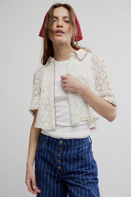 Woman wearing a white lace jacket, white shirt, and blue pinstripe pants on a plain background
