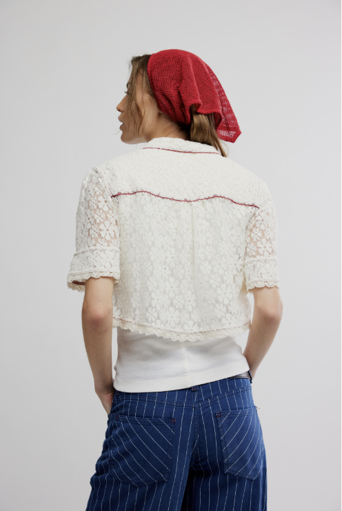 Person wearing a white lace top and blue striped pants with a red headscarf on a plain background