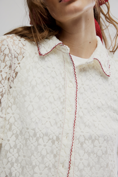 Close-up of a person wearing a white lace garment with red stitching.