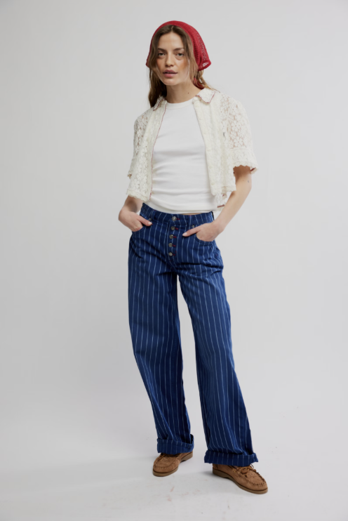 Woman wearing a white jacket, white shirt, blue striped pants, and brown shoes on a white background