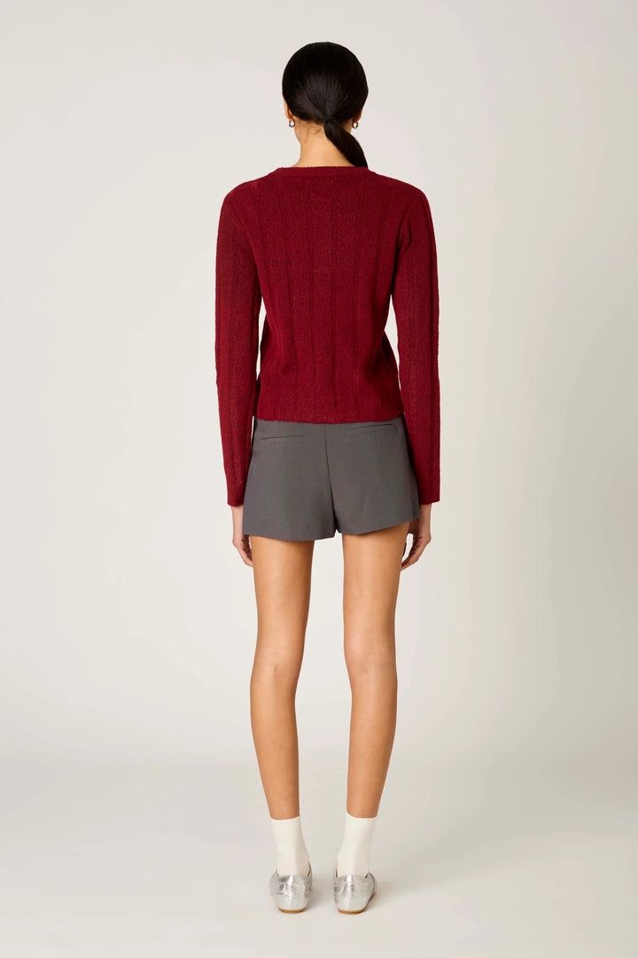 A model shown from the back wearing a burgundy ribbed knit long-sleeve top, gray shorts, white socks, and silver shoes against a light gray studio background.