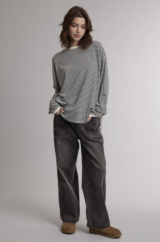 A woman modeling a black and white horizontally striped long-sleeve shirt with gathered cuffs, paired with dark gray wide-leg jeans and brown suede boots, against a neutral light gray studio background.