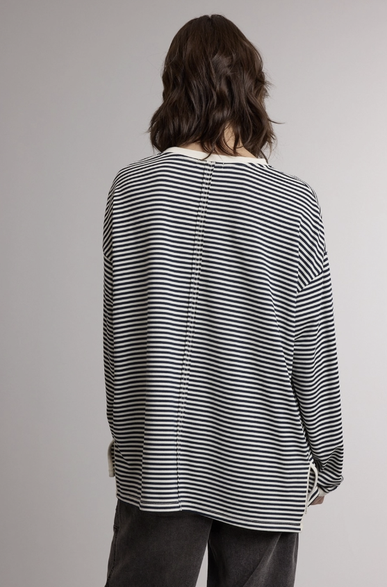 A person shown from the back wearing a black and white horizontally striped long-sleeve top and dark pants against a plain light gray studio background.