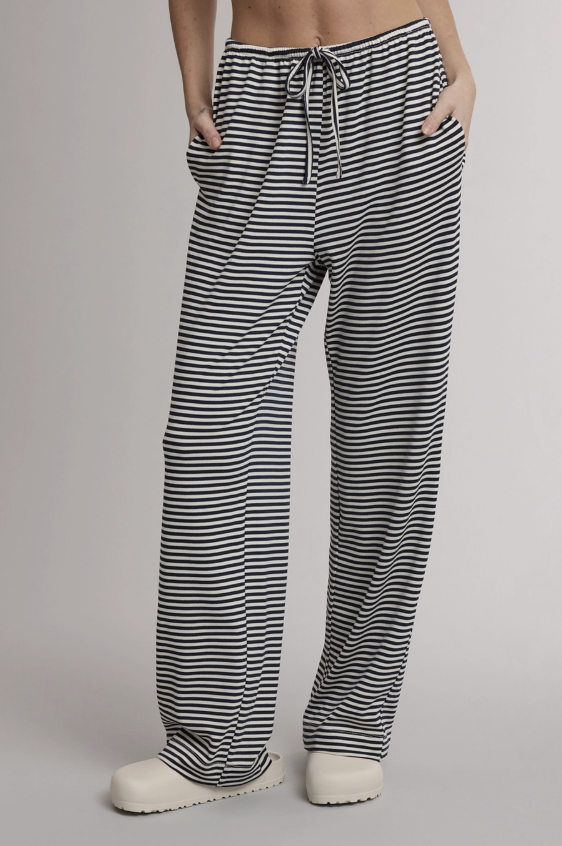 A person wearing loose black-and-white horizontally striped drawstring pants with side pockets, shown from the waist down against a light gray studio background.