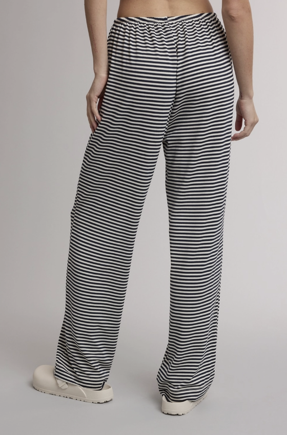 A person wearing loose black-and-white horizontally striped pants, shown from the waist down against a plain light gray studio background.