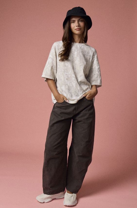 Woman wearing a light-colored top and dark pants against a pink background