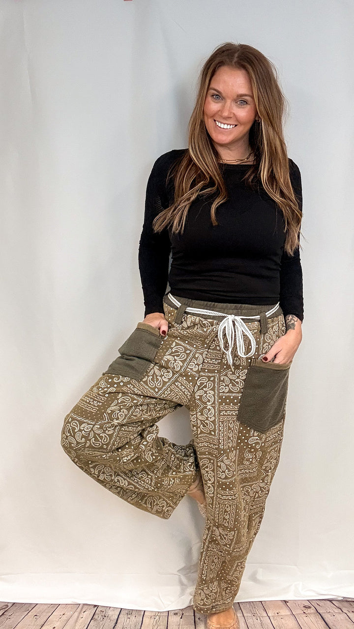Woman wearing olive green sweatpants with bandana print with black long sleeve top on white background
