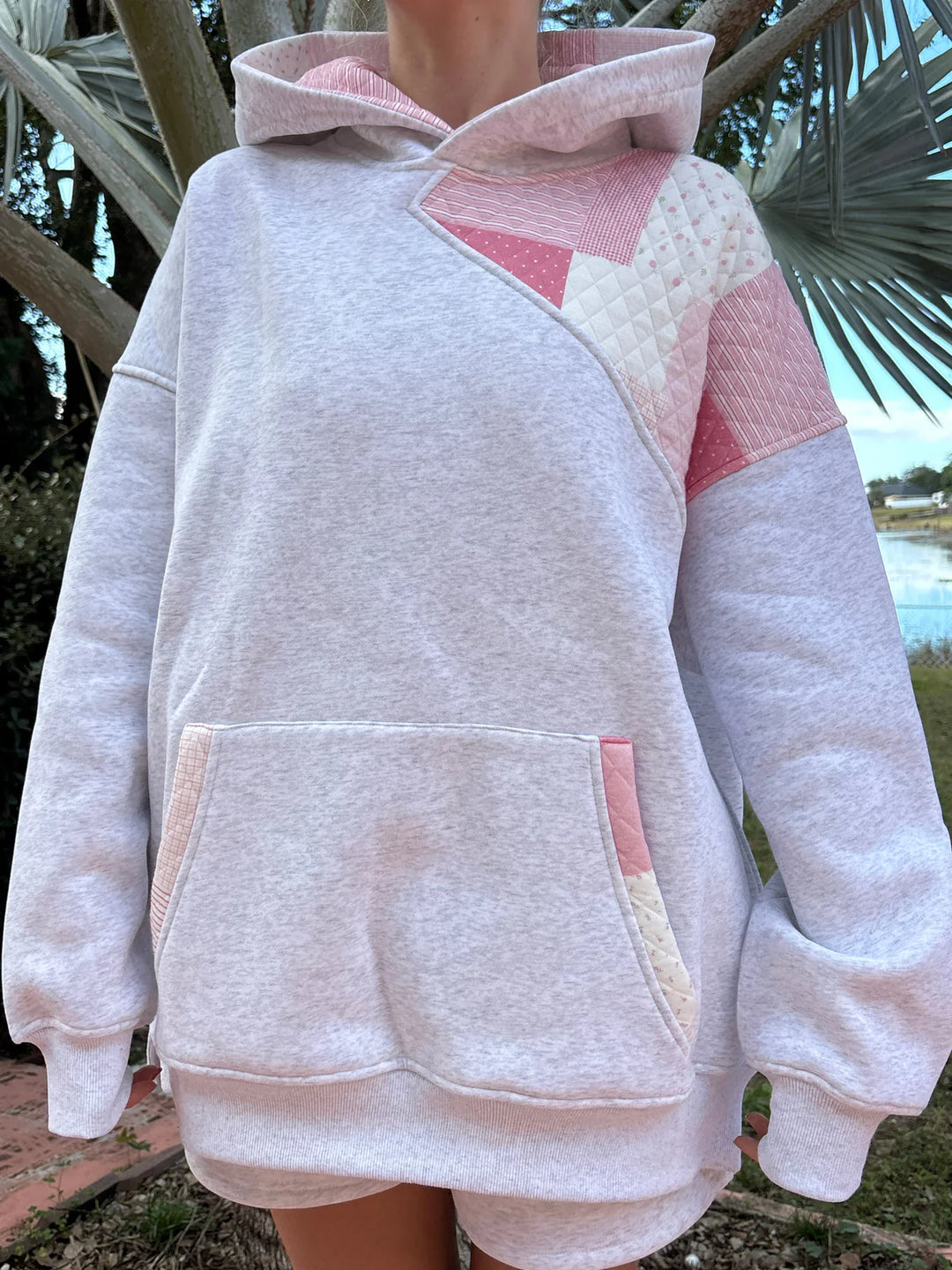 Person wearing grey hoodie with pink patchwork standing outdoors