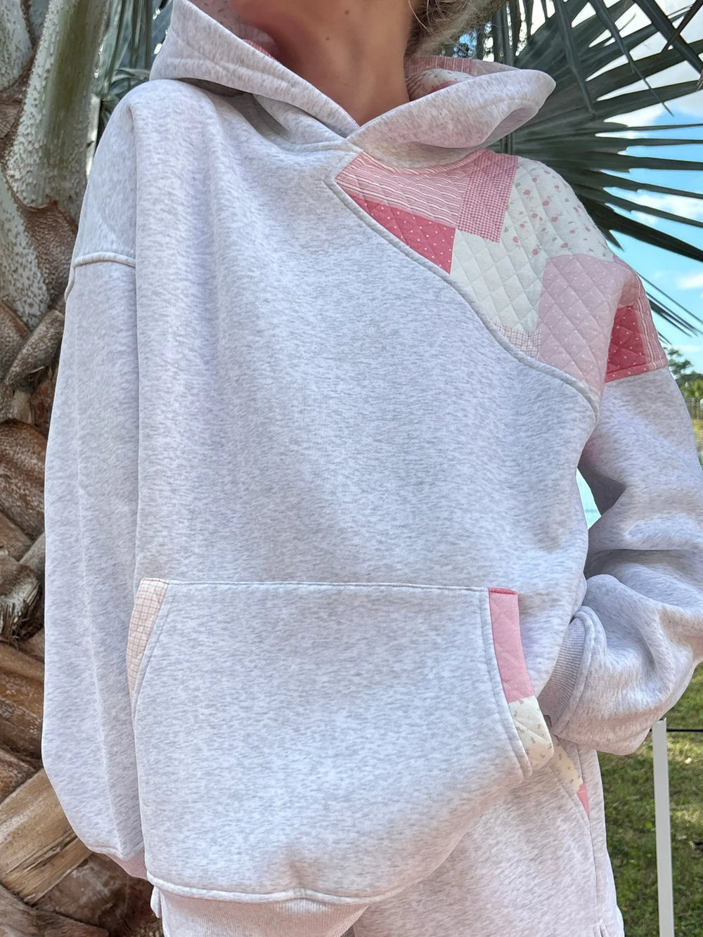 Person wearing grey sweatshirt with pink patchwork standing outdoors