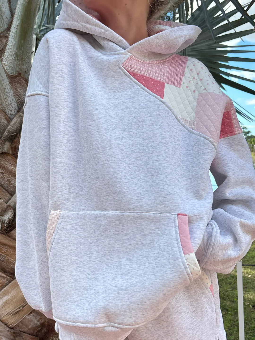 Person wearing grey sweatshirt with pink patchwork standing outdoors