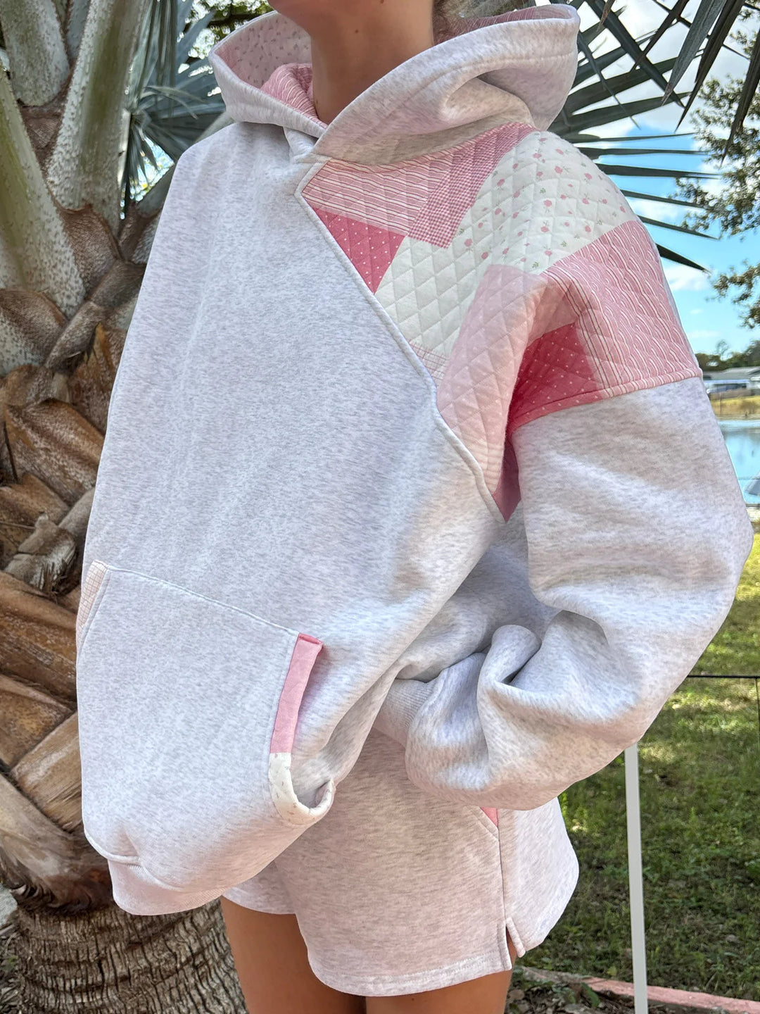 Person wearing grey sweatshirt with pink patchwork standing outdoors