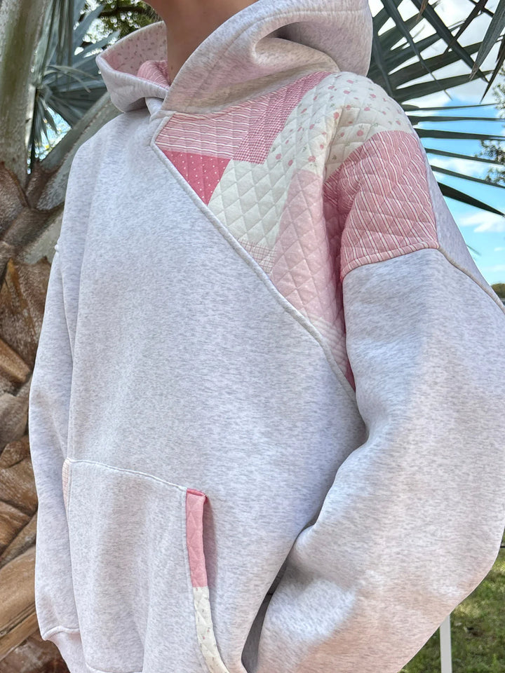 Person wearing grey sweatshirt with pink patchwork standing outdoors