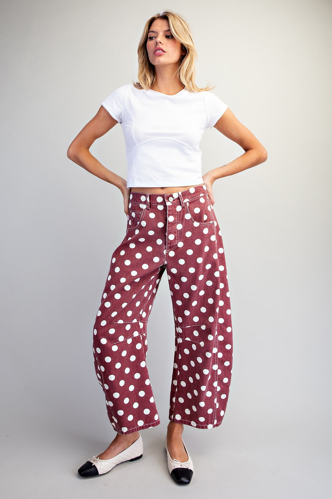 Woman wearing a white top and red polka dot pants on a plain background