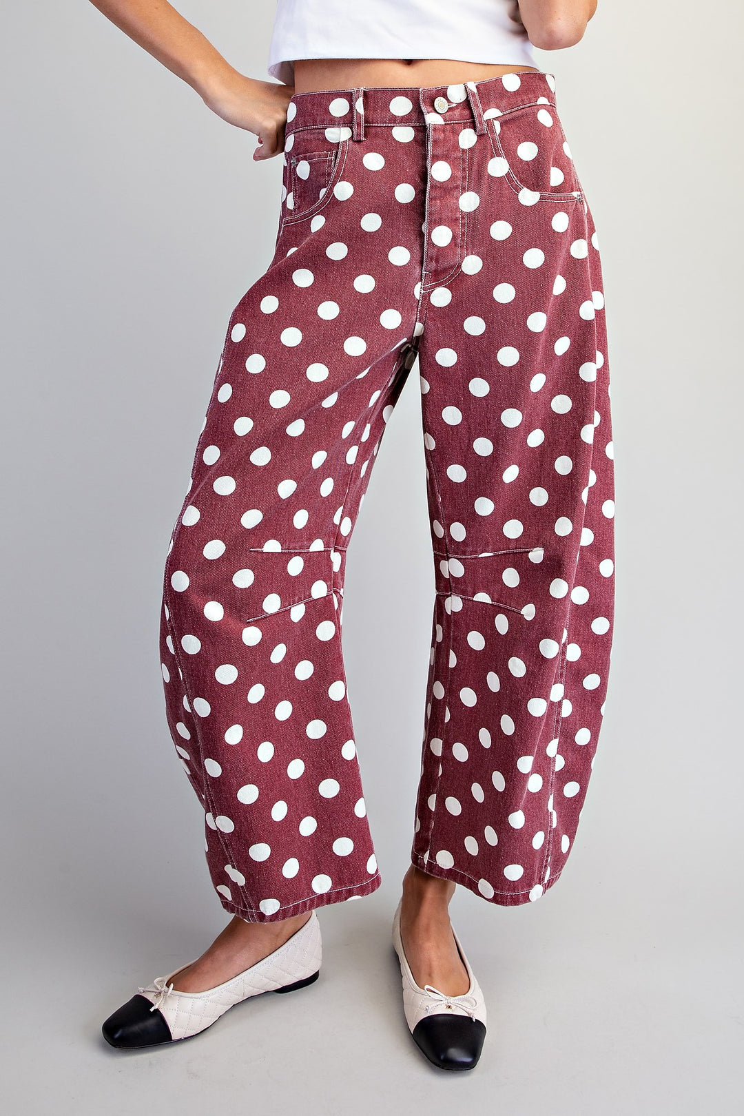 A person wearing wide-leg cropped pants in a dusty rose color with a white polka dot pattern, paired with black and white flat shoes, against a light gray studio background.