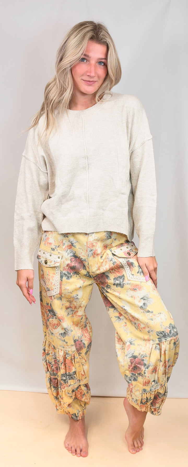 A woman modeling a two-piece loungewear set consisting of a cream-colored long-sleeve top and yellow floral harem pants, standing against a light beige studio backdrop.