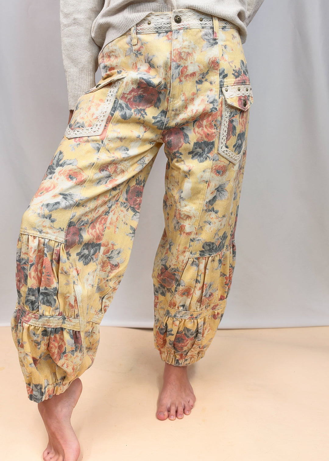 A person wearing loose, balloon-style pants with a vintage floral print in yellow, orange, and blue, paired with a light gray sweatshirt, shown from the waist down against a plain studio backdrop.