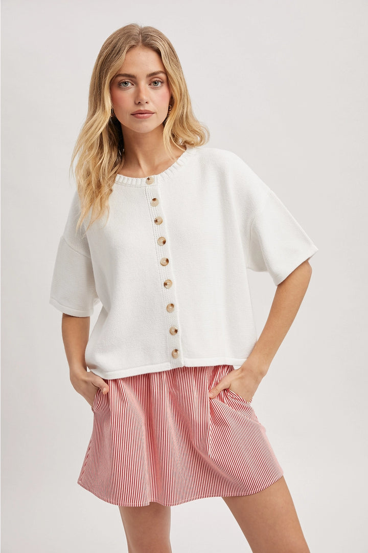 Woman wearing white button up cardigan with red skirt on plain background