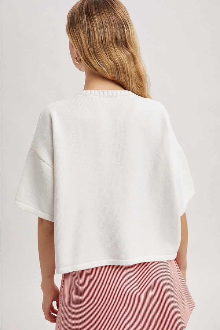 Back of woman wearing white cardigan and red skirt on plain background