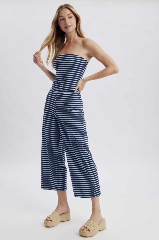 Woman wearing a strapless navy and white striped jumpsuit on a light gray background