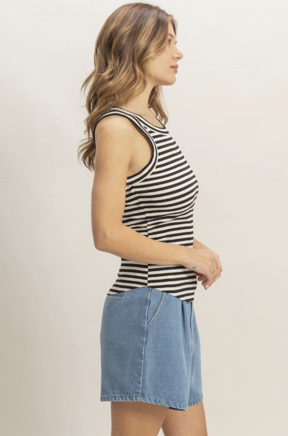 Woman wearing a black and white striped tank top and denim skirt on a beige background