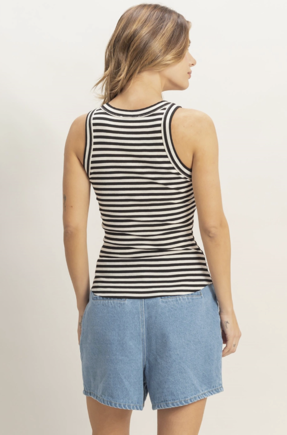 Woman wearing a black and white striped tank top and denim shorts on a plain background