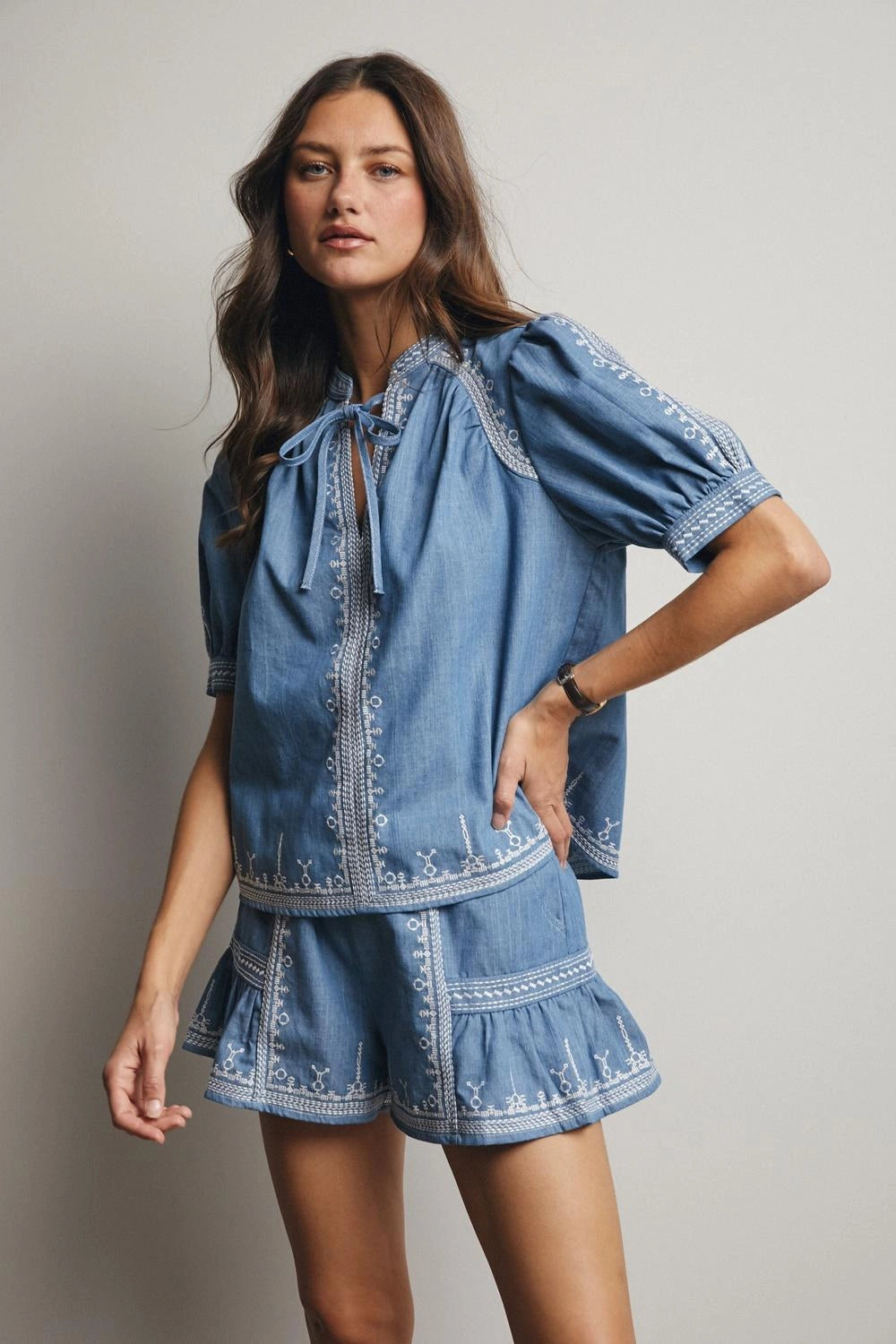 Woman wearing a blue denim outfit with embroidery on a plain background