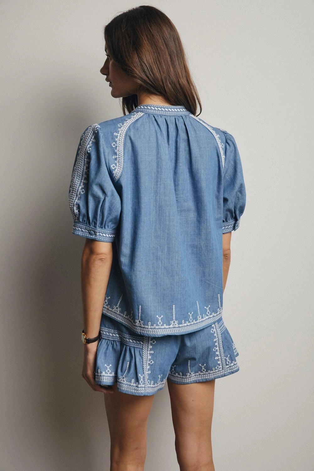 Woman wearing a blue denim outfit with embroidered details on a plain background
