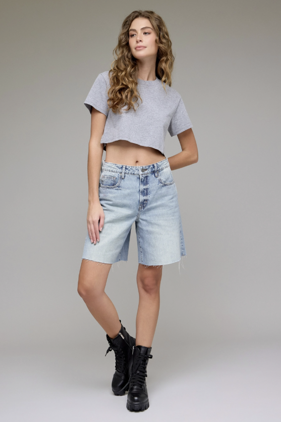 Woman wearing a gray crop top and denim shorts on a plain background