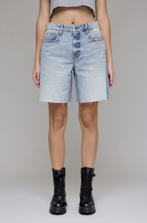 Person wearing light blue denim shorts and black boots on a plain background