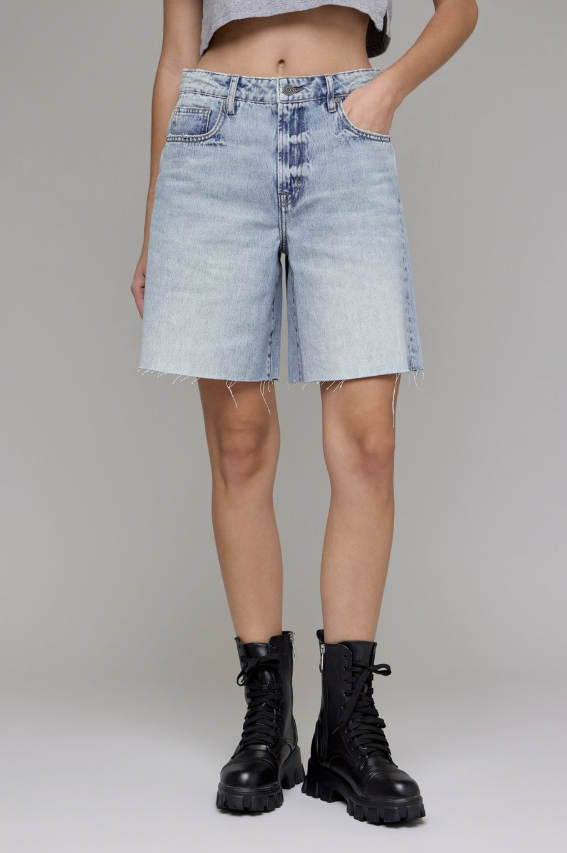 Person wearing light blue denim shorts and black boots on a plain background