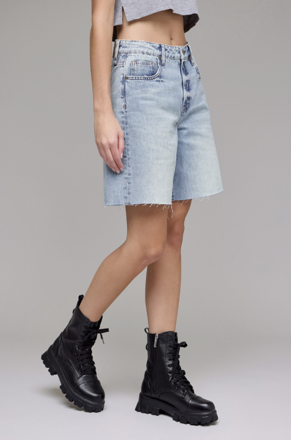 Person wearing light blue denim shorts and black combat boots on a plain background