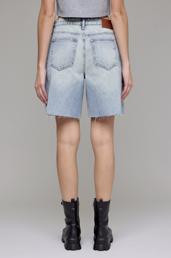 Person wearing light blue denim shorts and black boots on a plain background