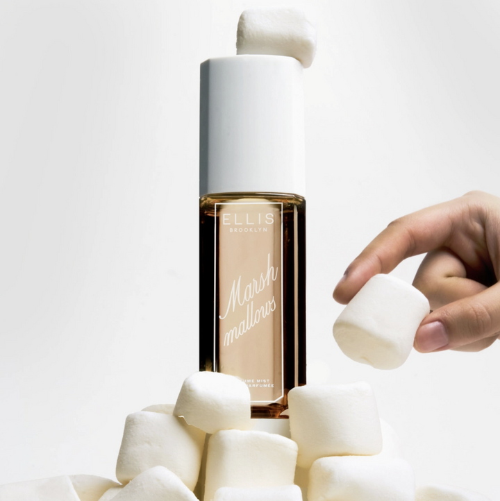 Ellis Essentials Marshmallows liquid foundation bottle surrounded by white marshmallows, with a hand holding a marshmallow on a clean white background.