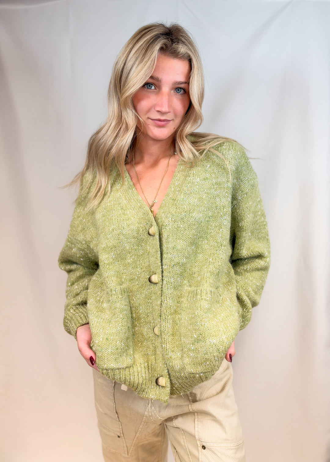 Woman wearing green cardigan sweater with beige pants on plain background