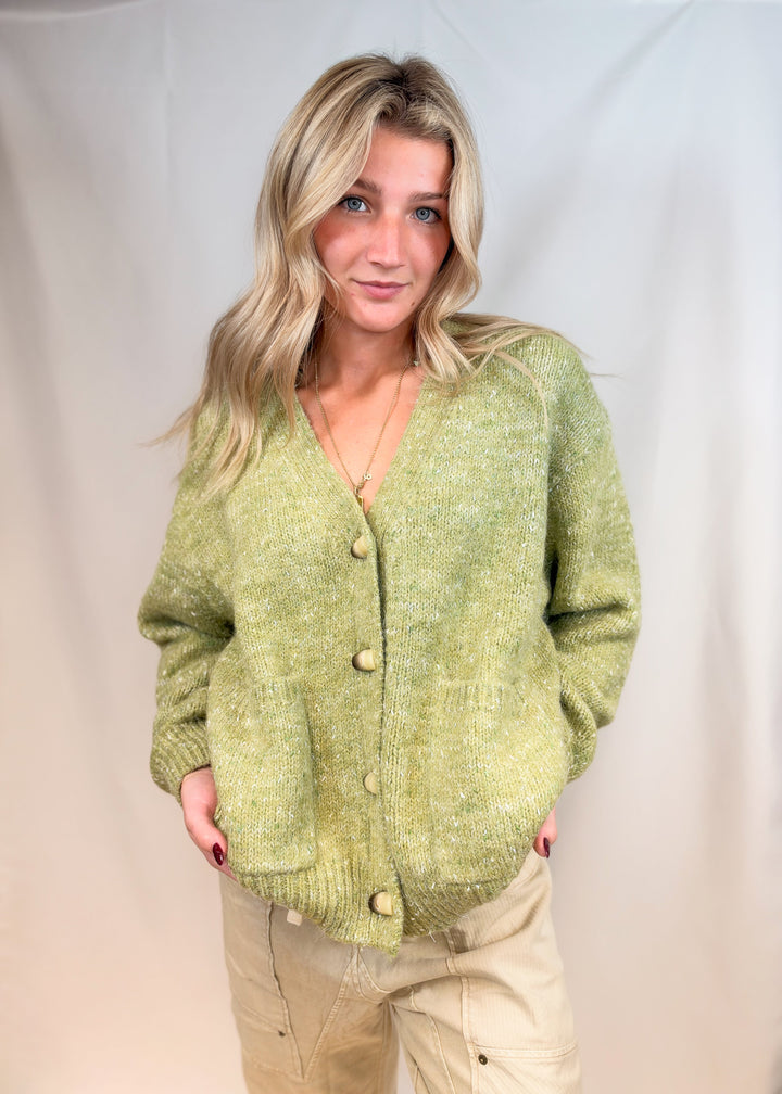 Woman wearing green cardigan sweater with beige pants on plain background
