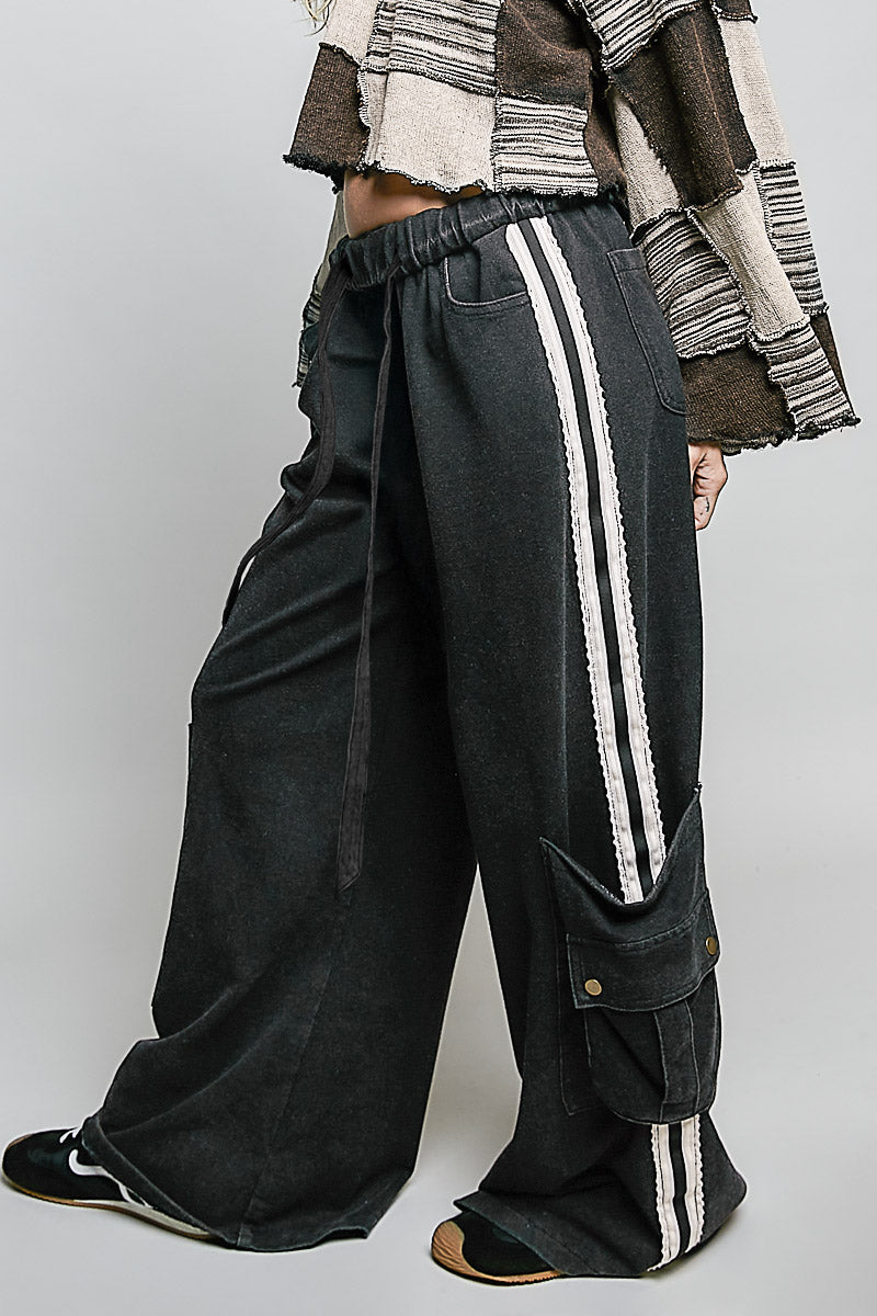 Person wearing black wide-leg pants with white stripes and a patterned jacket on a plain background