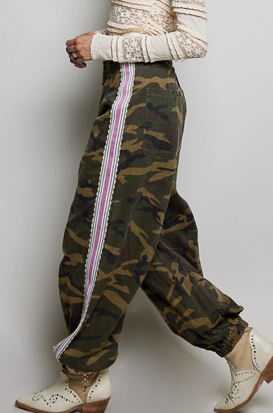 Woman wearing camo pants with pink ribbon detail on plain background