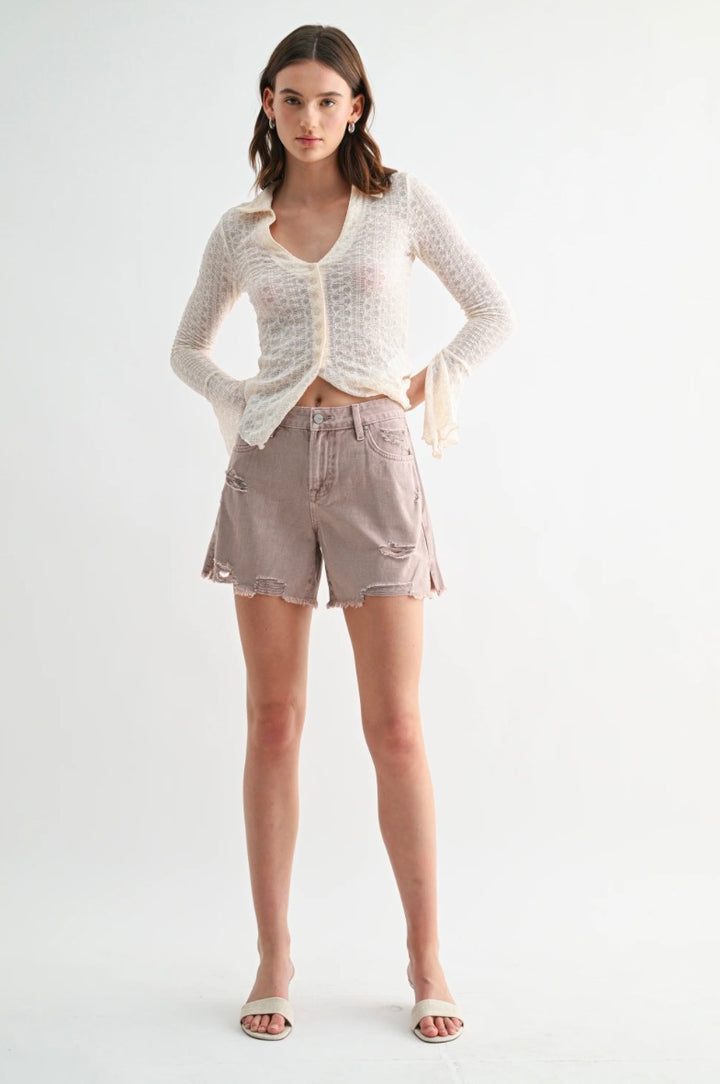 Woman wearing a white knit cardigan and beige shorts on a white background