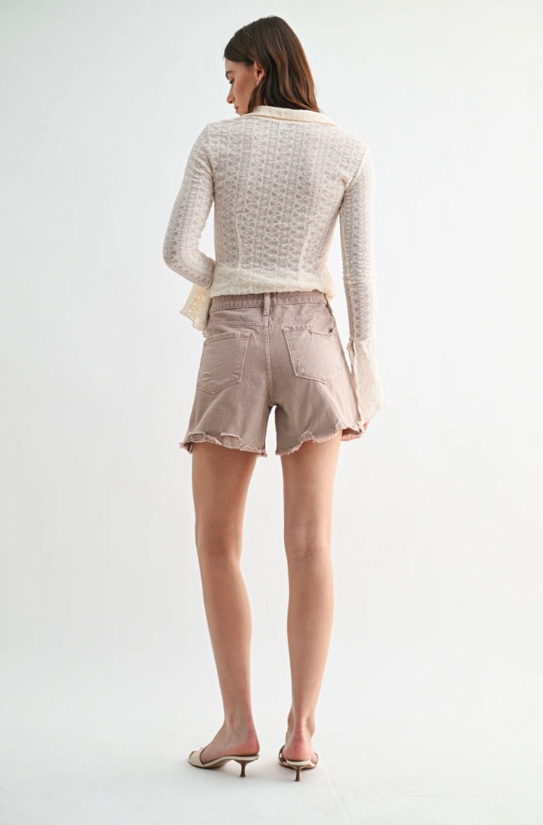 Woman wearing a light gray textured sweater and beige shorts on a white background