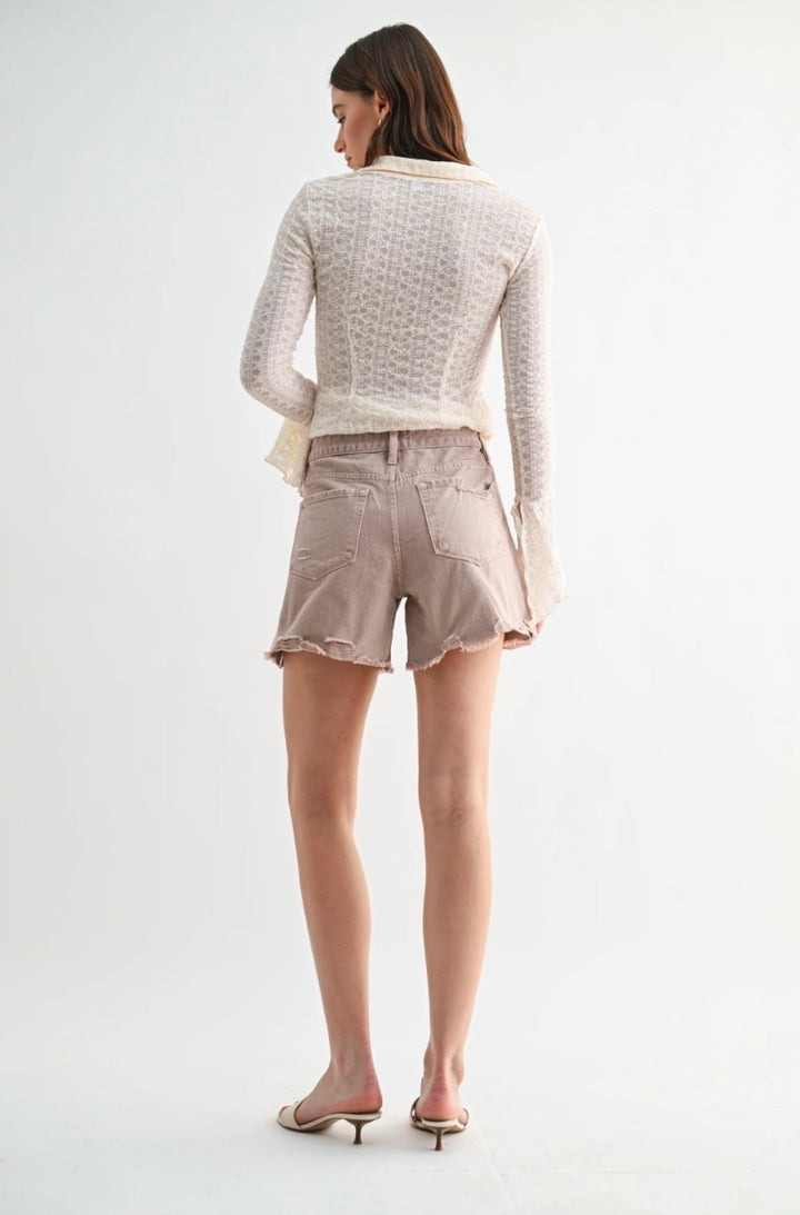 Woman wearing a light gray textured sweater and beige shorts on a white background