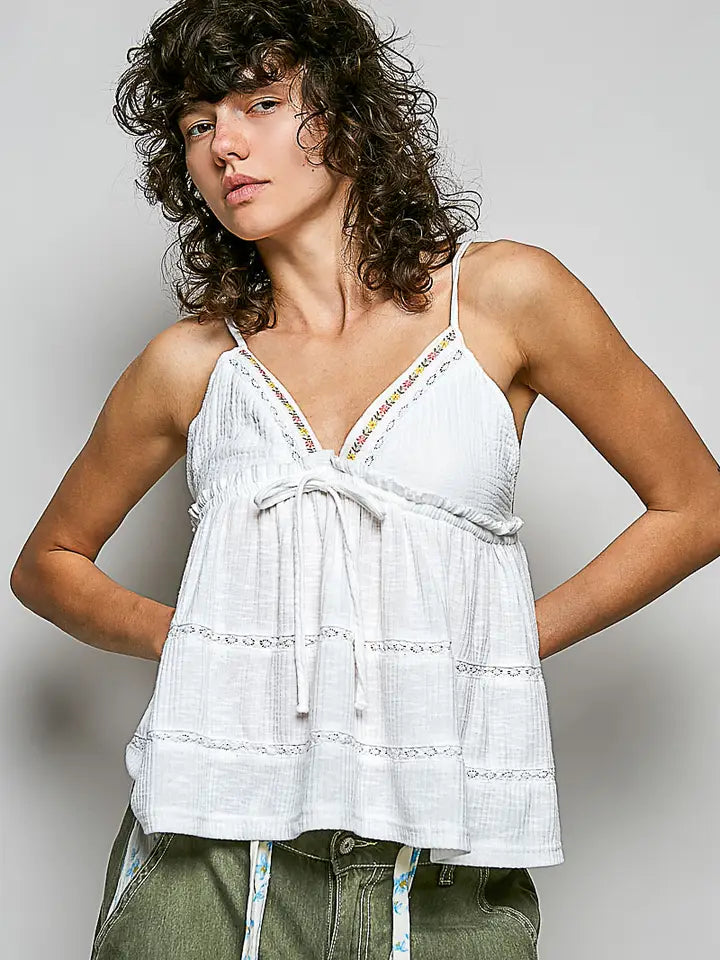 Woman wearing a white sleeveless top with green pants against a plain background